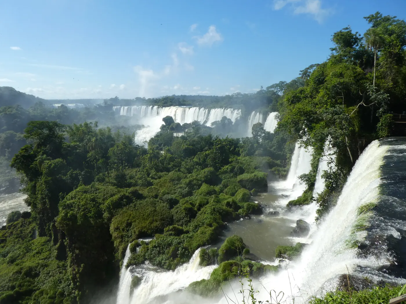 The Iguazu Falls pouring through dense green rainforest under a blue sky